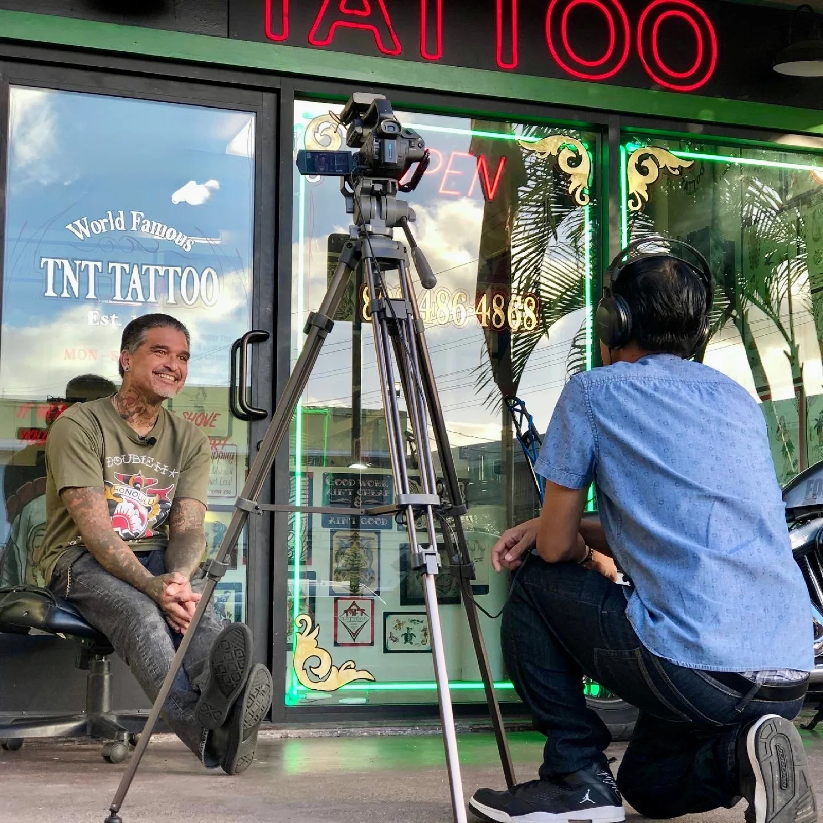 Kevin Mokuahi being interviewed on camera outside TNT Tattoo in Aiea — green shirt, calm posture